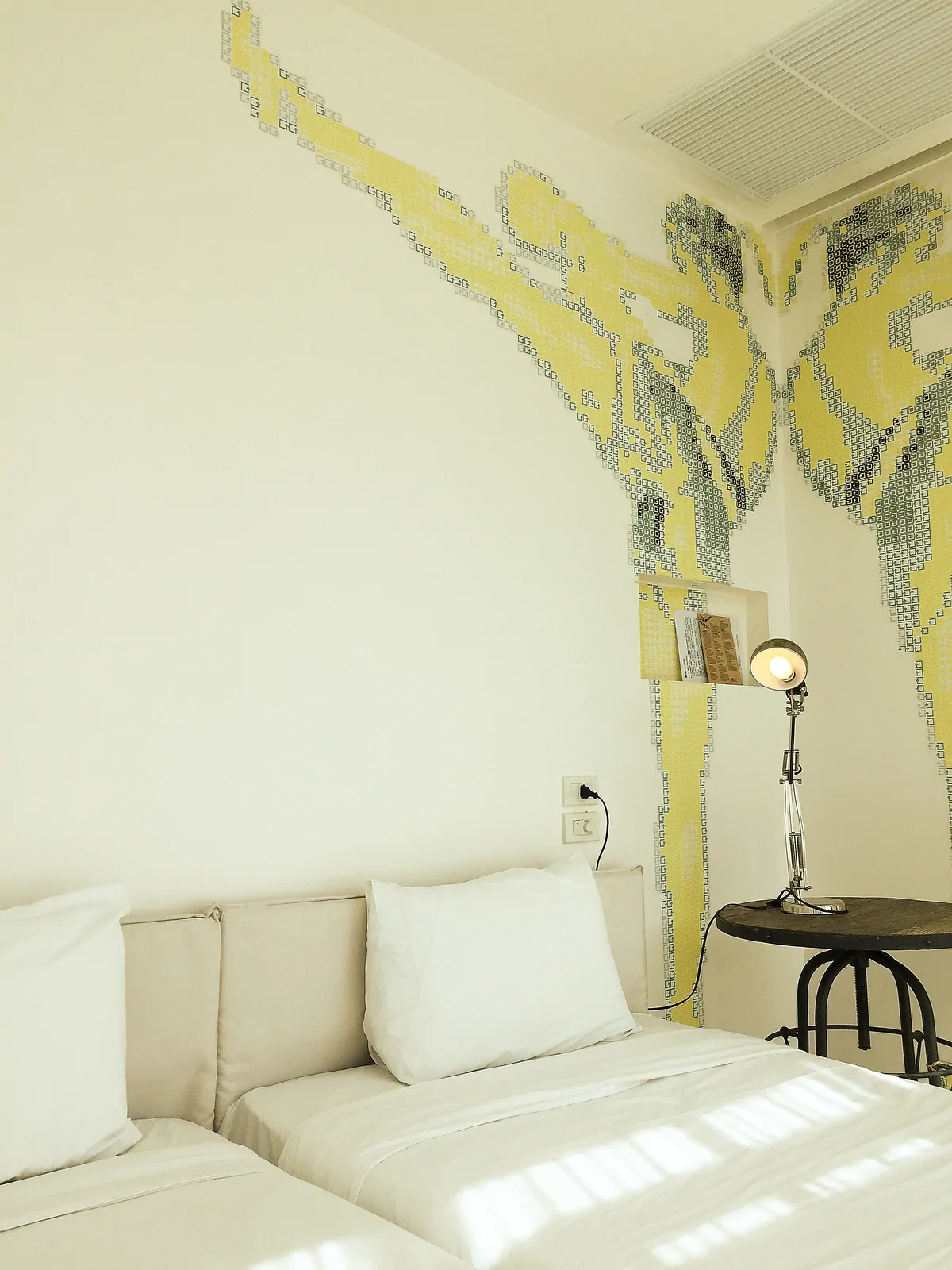 Two beds side by side beneath a tiled mural with a table lamp